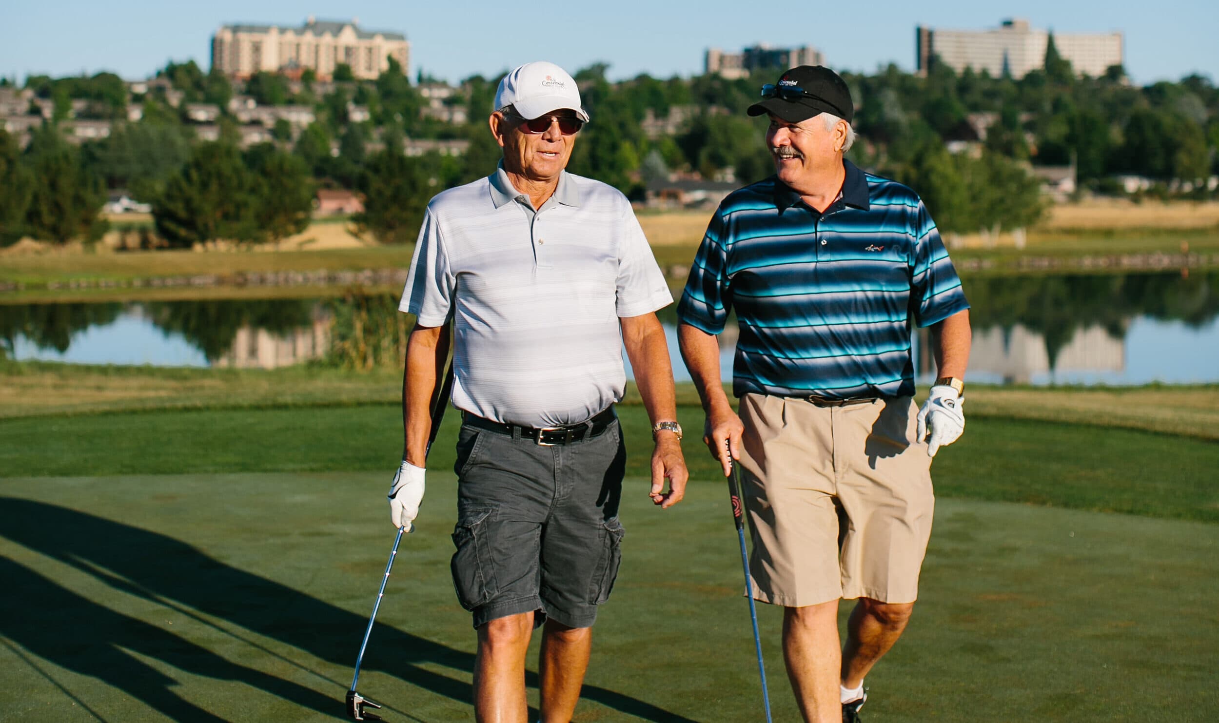 Two friends walk and talk on a golf course.